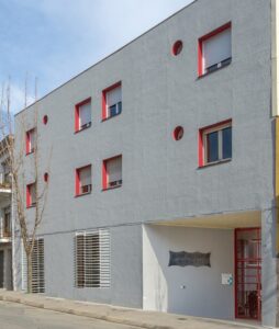 Façana d'edifici modern gris amb detalls vermells, finestres amb persianes i Centre Sociosanitari Verge del Puig