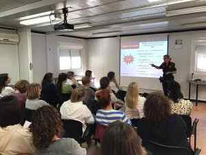 Agent de policia impartint una xerrada de seguretat a un grup de dones en una aula amb projector i pantalla.