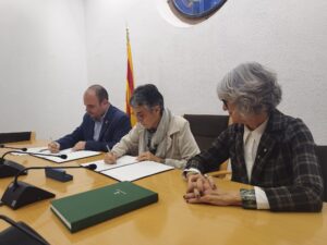 Tres persones signant documents oficials en una sala de reunions amb bandera catalana de fons