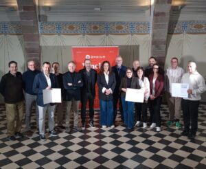 Grup de professionals posant amb certificats davant banner d'Omnium en sala amb decoració modernista