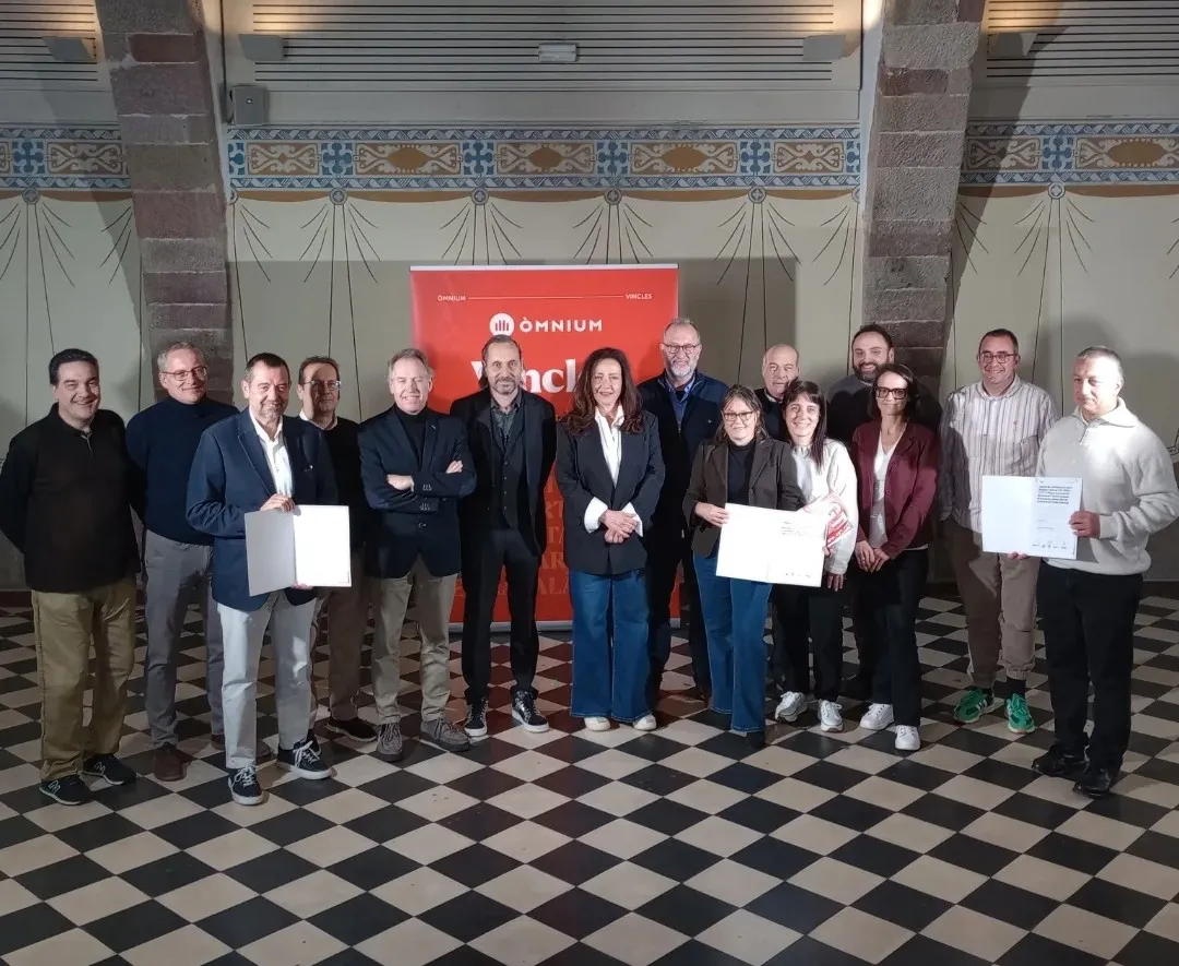 Grup de professionals posant amb certificats davant banner d'Omnium en sala amb decoració modernista