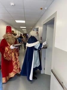 Dos homes disfressats de Reis Mags visitant un hospital, portant regals pels pacients durant les festes nadalenques.
