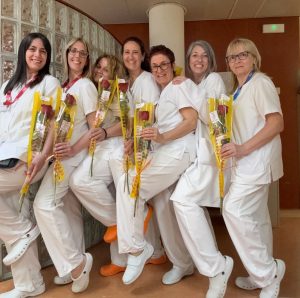 Grup d'infermeres amb uniforme blanc sostenint flors grogues en un hospital, celebrant una ocasió especial