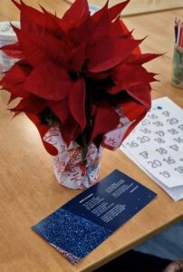 Flor de pascua roja en jarrón decorativo sobre mesa con calendario y tarjeta navideña azul con estrellas