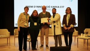 Cinc persones en una cerimònia de lliurament del Premi d'Innovació Xarxa C17, posant amb un certificat al centre de l'escenari.