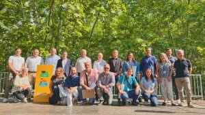 Grup de professionals posant per a foto grupal a l'aire lliure amb cartell taronja de Sant Celoni al fons entre vegetació verda