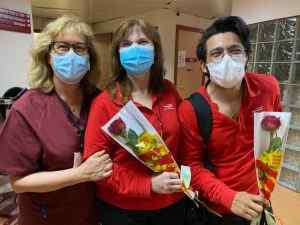 Tres dones amb mascaretes somriuen mentre sostenen roses roges en un edifici d'oficines.