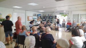 Concert de música en viu per a gent gran en centre de dia amb assistència asseguda i músics actuant