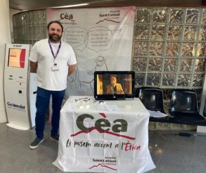 Representant del CEA davant d'un estand informatiu sobre ètica hospitalària amb pantalla i materials a l'Hospital Sant Celoni
