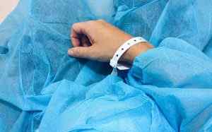 Mà de pacient amb polsera d'identificació hospitalària sobre roba quirúrgica blava en entorn mèdic